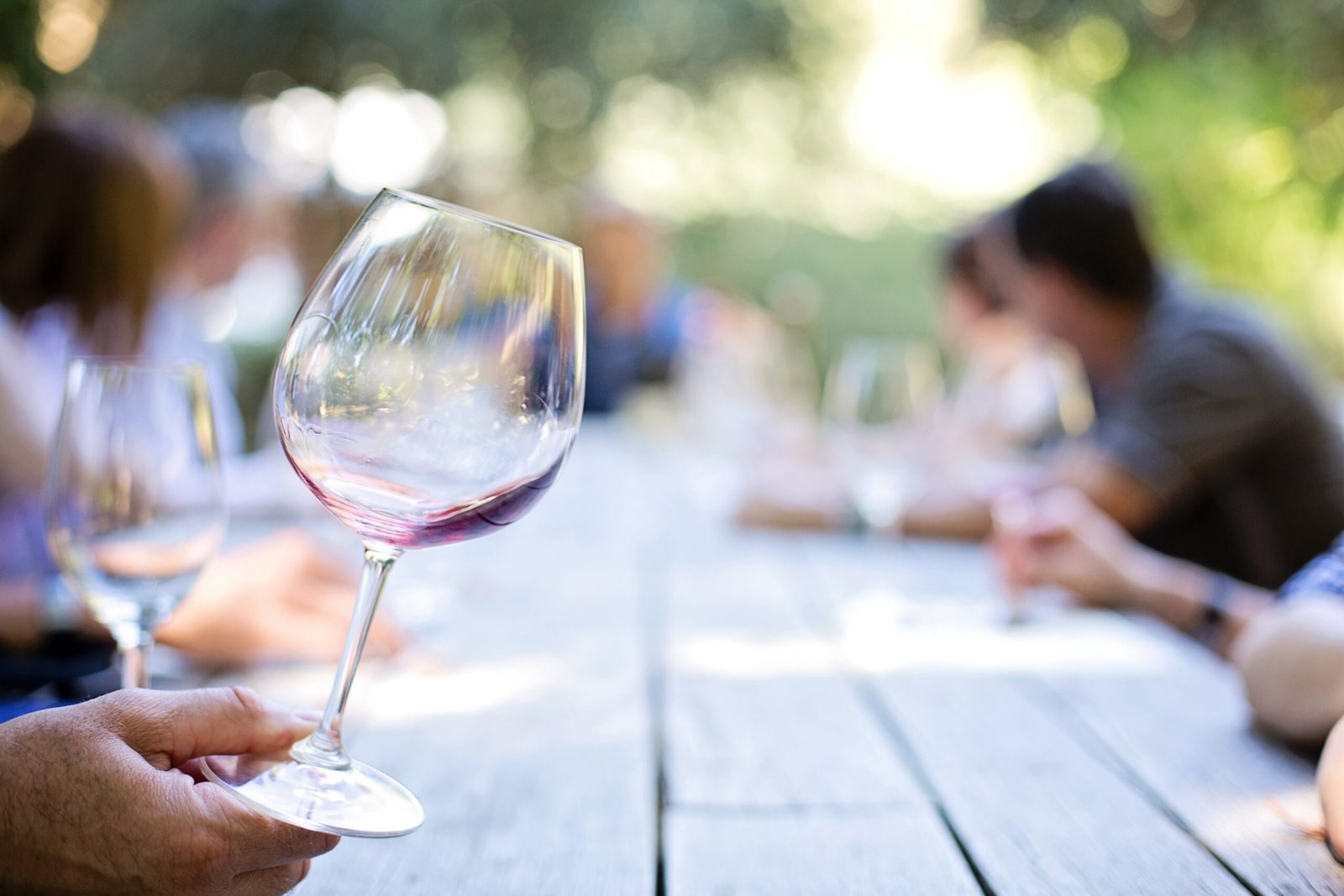 Copa de vino tinto sujeta por el tallo sobre una mesa de madera al aire libre