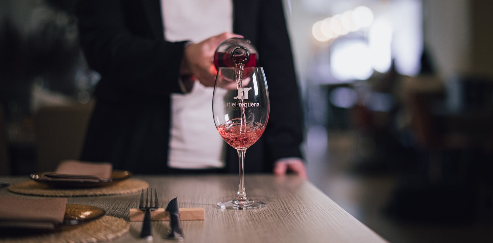 Sirviendo una copa de vino tinto en una mesa puesta con cubiertos
