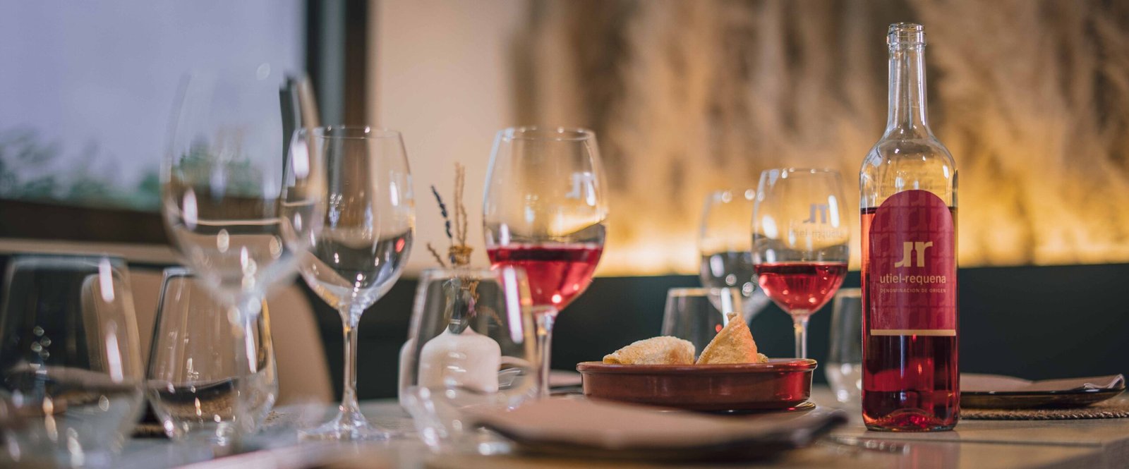 Mesa preparada con copas de vino blanco, rosado y tinto junto a varios platos