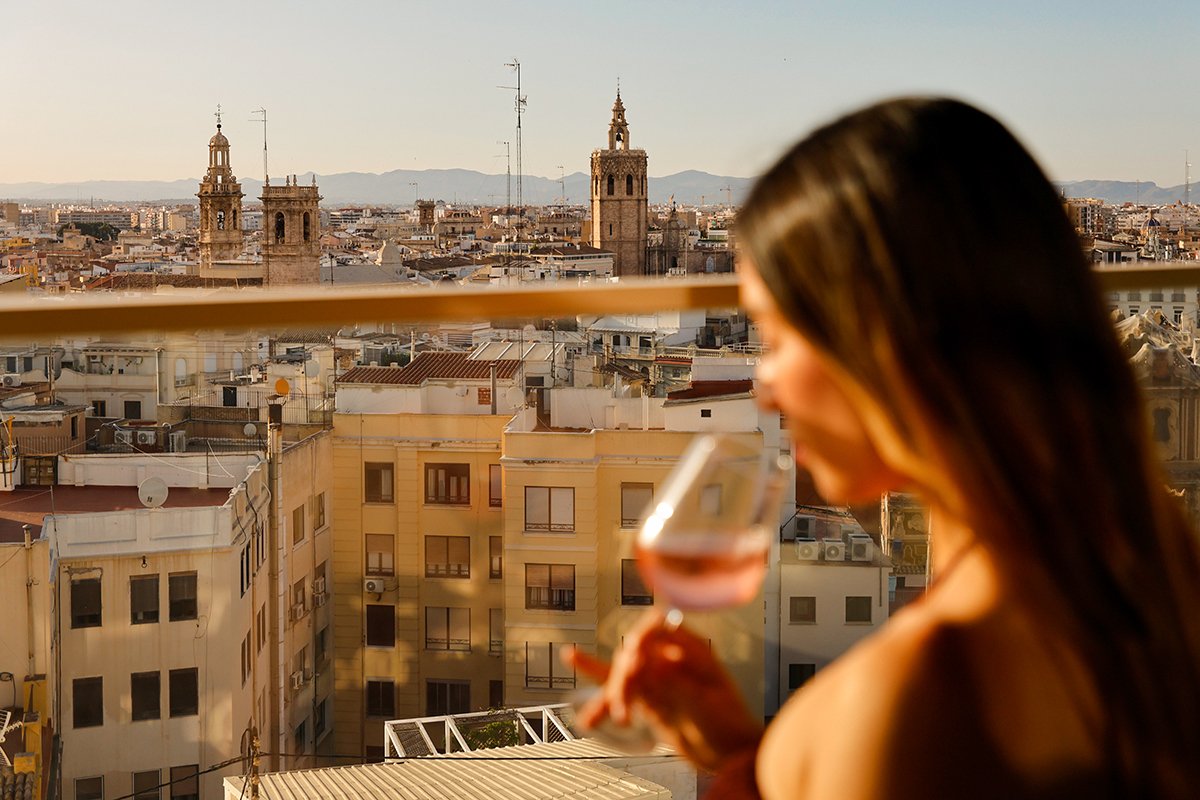 Mujer con una copa de vino blanco en una terraza con los tejados de Valencia al fondo