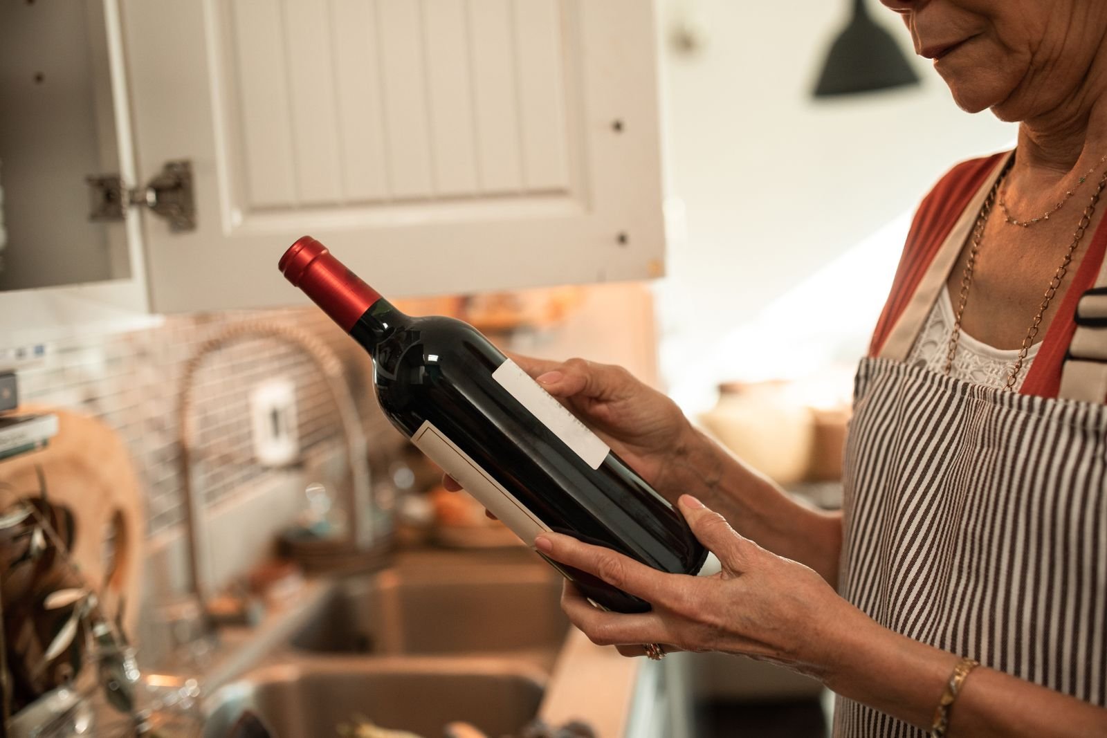 Mujer en la cocina sujetando una botella de vino empezada junto a los fogones