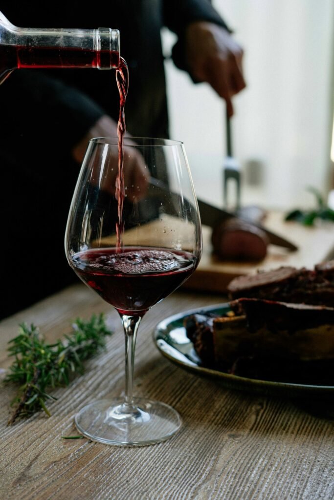 Copa de vino tinto de la DO Utiel-Requena servida junto a un plato de carne en una mesa rústica