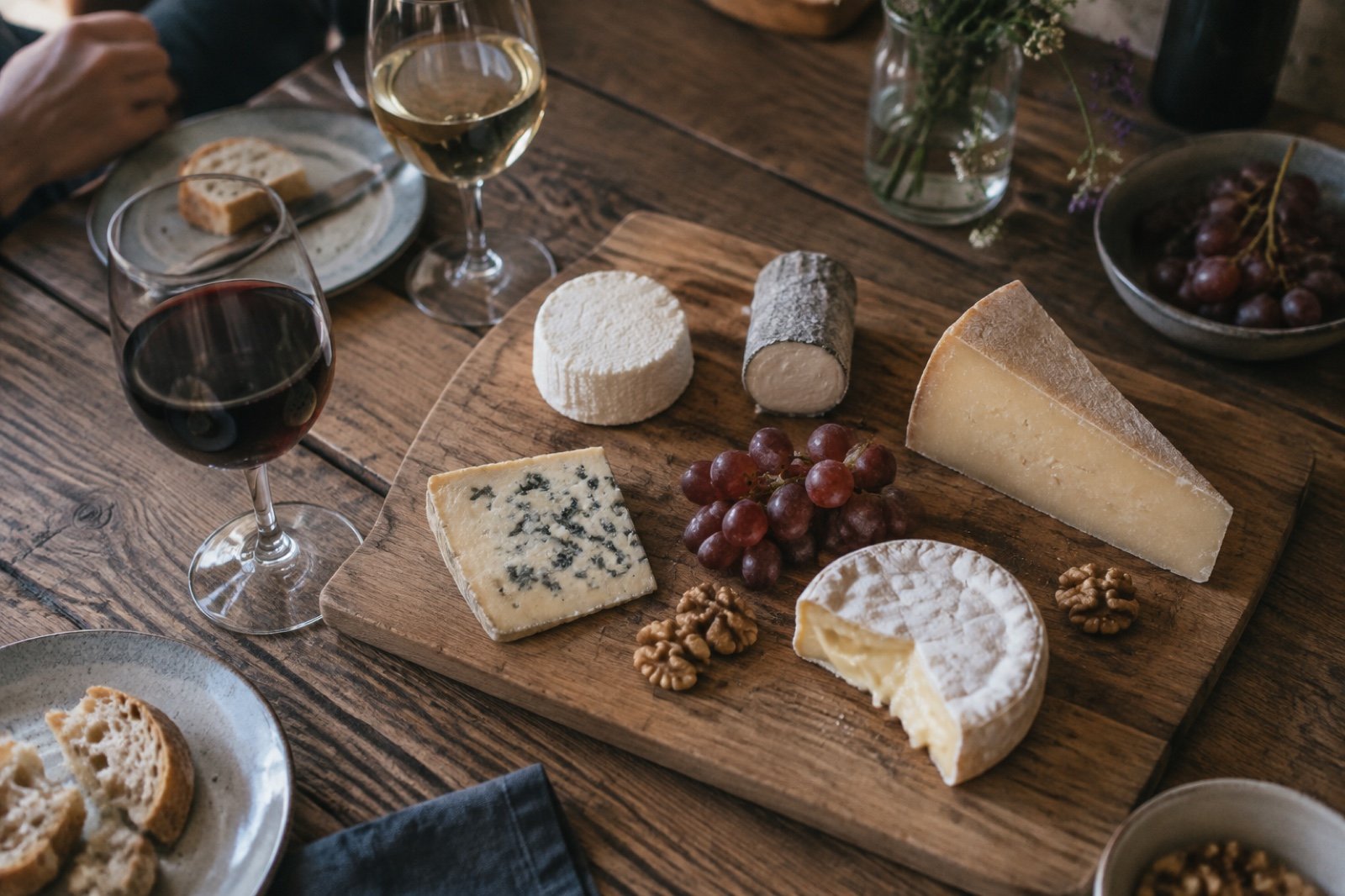 Tabla de madera con cinco quesos distintos, uvas, nueces y dos copas de vino, una de tinto y otra de blanco